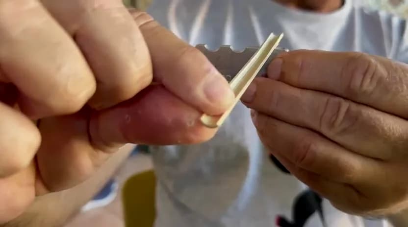 Maker cleaning the edges of split oboe cane with a blade